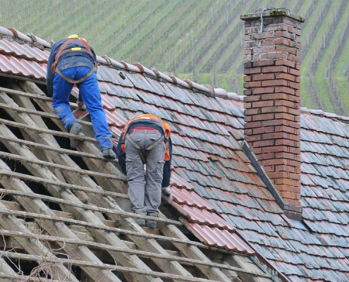 two person putting roof tiles on roof at daytime